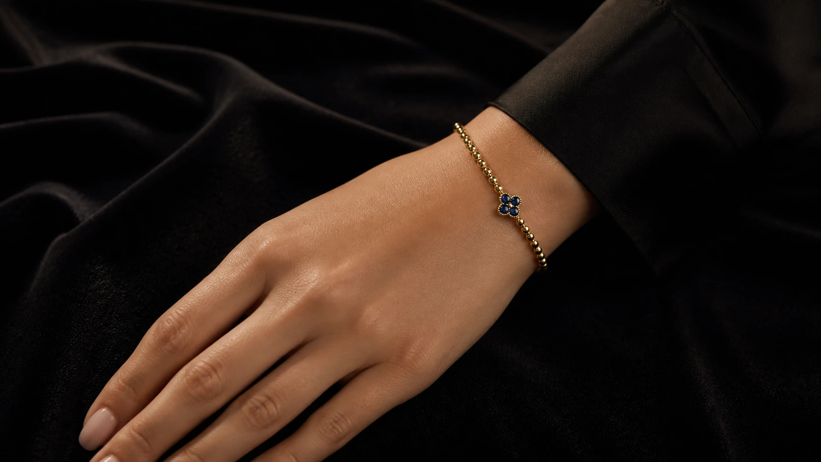 Mano de modelo con pulsera dorada y piedras azules